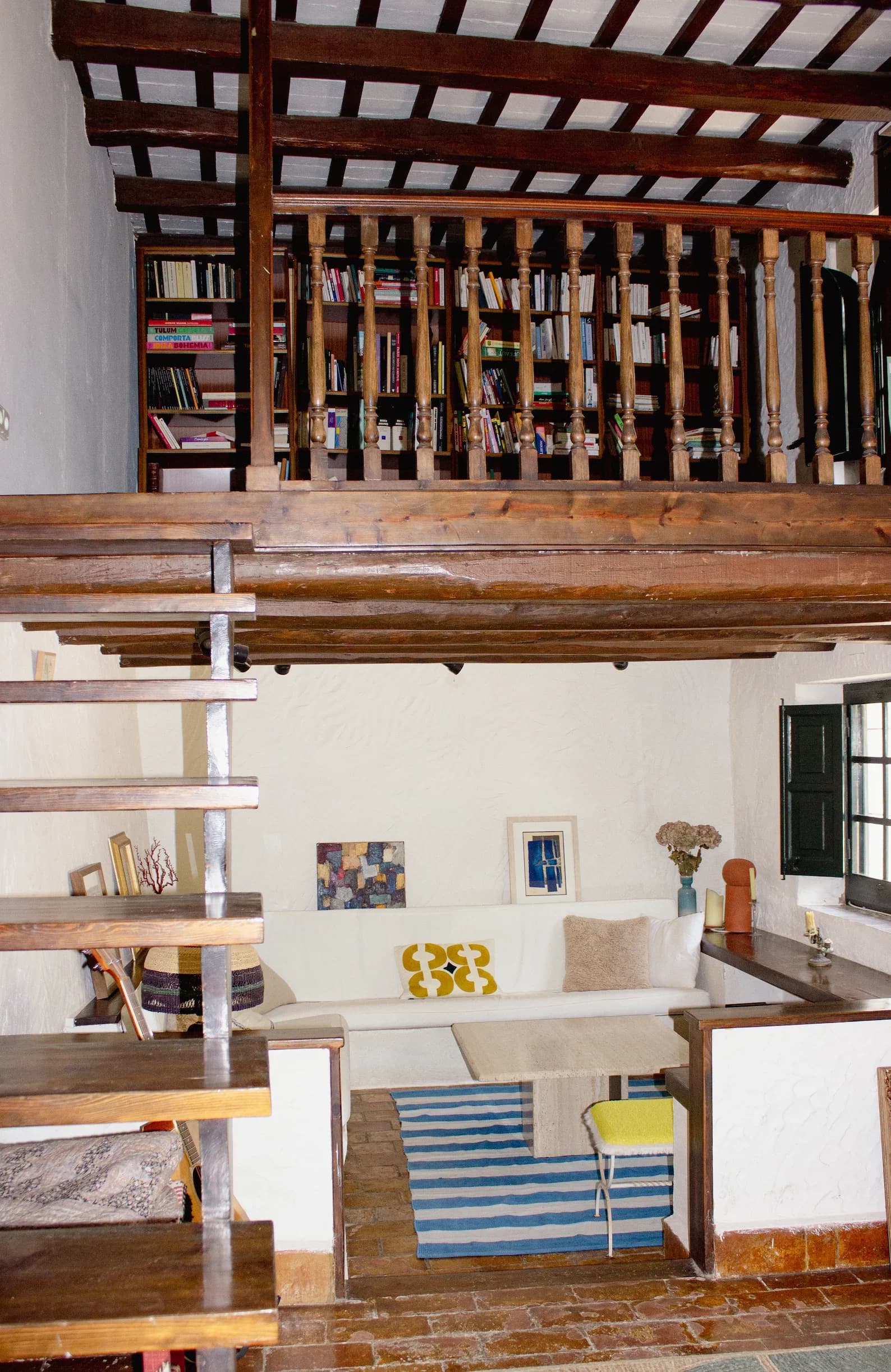 Living room with mezzanine library and wooden staircase at Masia Can Pares